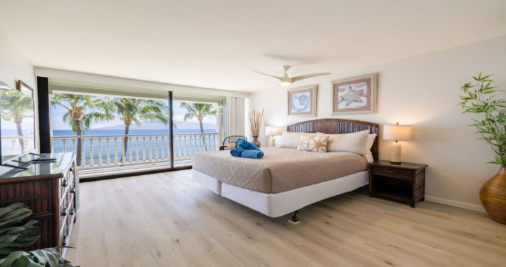 spacious room with bed, dresser, night stands with lamps and large sliding doors to the lanai