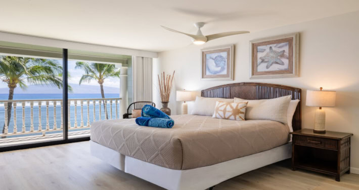 spacious room with bed and two night stands that look out to the private lanai overlooking the ocean